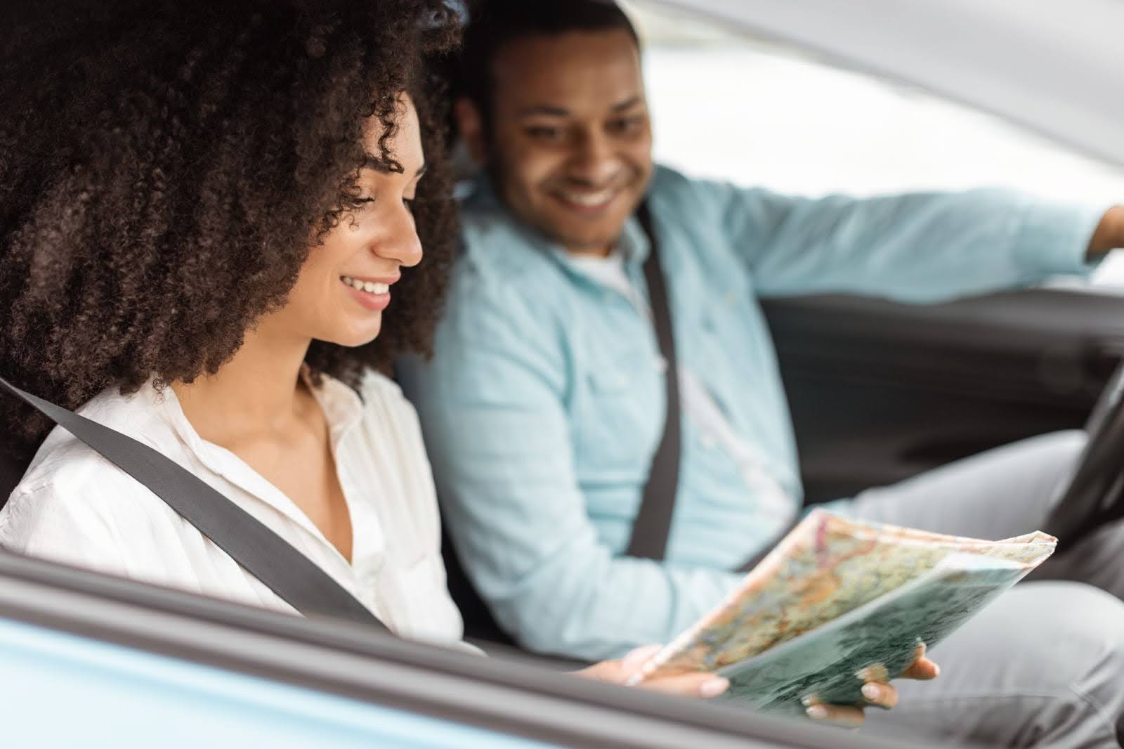 Smiling woman in the passenger seat reads a map while a man drives, both wearing seatbelts inside a car&mdash;an ideal scene for efficient routes managed with Transportation Dispatch Software.