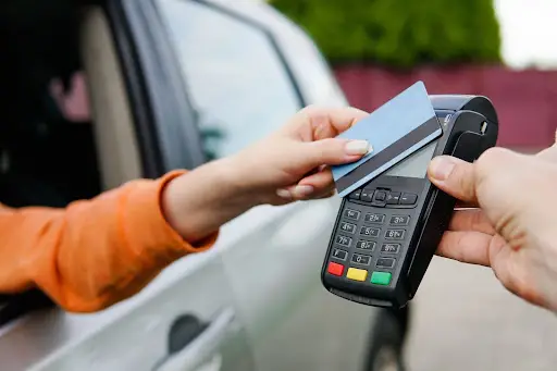 A person in a car pays with a credit card using contactless payment on a card reader held by another person outside the vehicle.