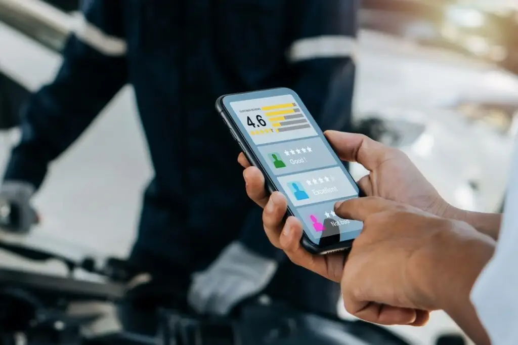 Close-up of a person using a smartphone to view and rate profiles with star ratings, while another stands near a car with its hood open&mdash;illustrating how PerGo transportation dispatch software streamlines NEMT services and improves user experiences.