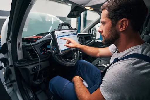 A man sits in the driver&rsquo;s seat of a car, using transportation management software on a diagnostic tablet mounted to the steering wheel to check vehicle data. He is focused and appears to be working or troubleshooting.