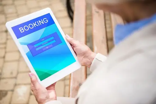 A person holds a tablet outdoors displaying a booking screen with login and password fields, showcasing an advanced NEMT Software solution for efficient transportation management.