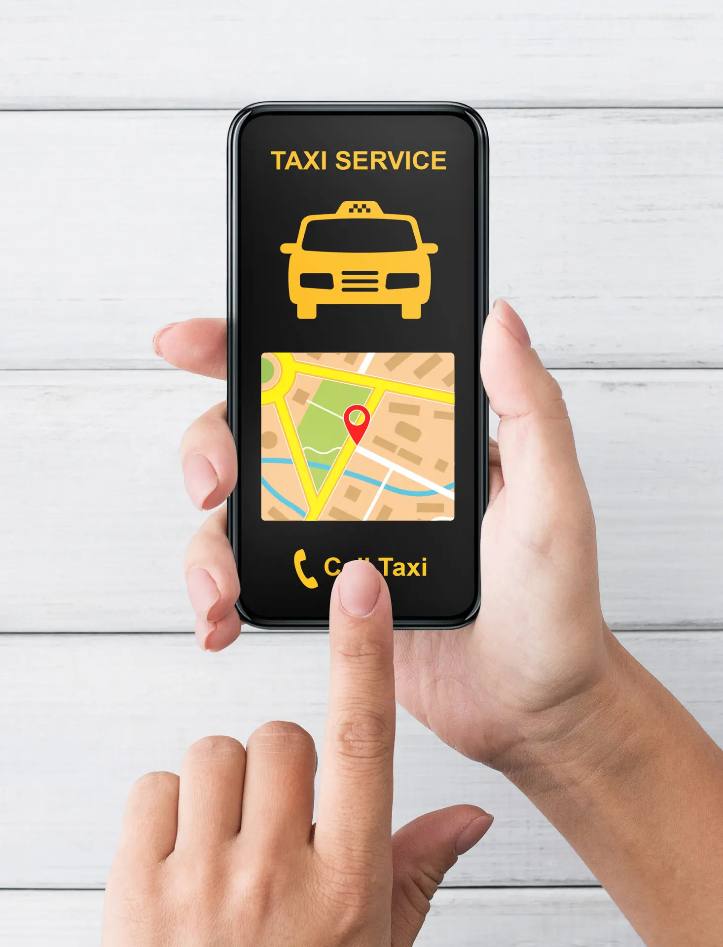 A person holding a smartphone with a TAXI SERVICE app open, showing a taxi icon, a map with a location pin, and a Call Taxi button on the screen. The phone is held over a white wooden surface.