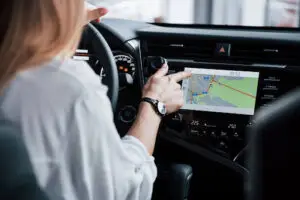 A person sitting in a car uses the touchscreen navigation system on the dashboard, with a digital map and directions displayed on the screen.